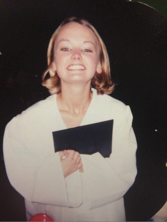 Girl in graduation gown holding diploma with a big smile