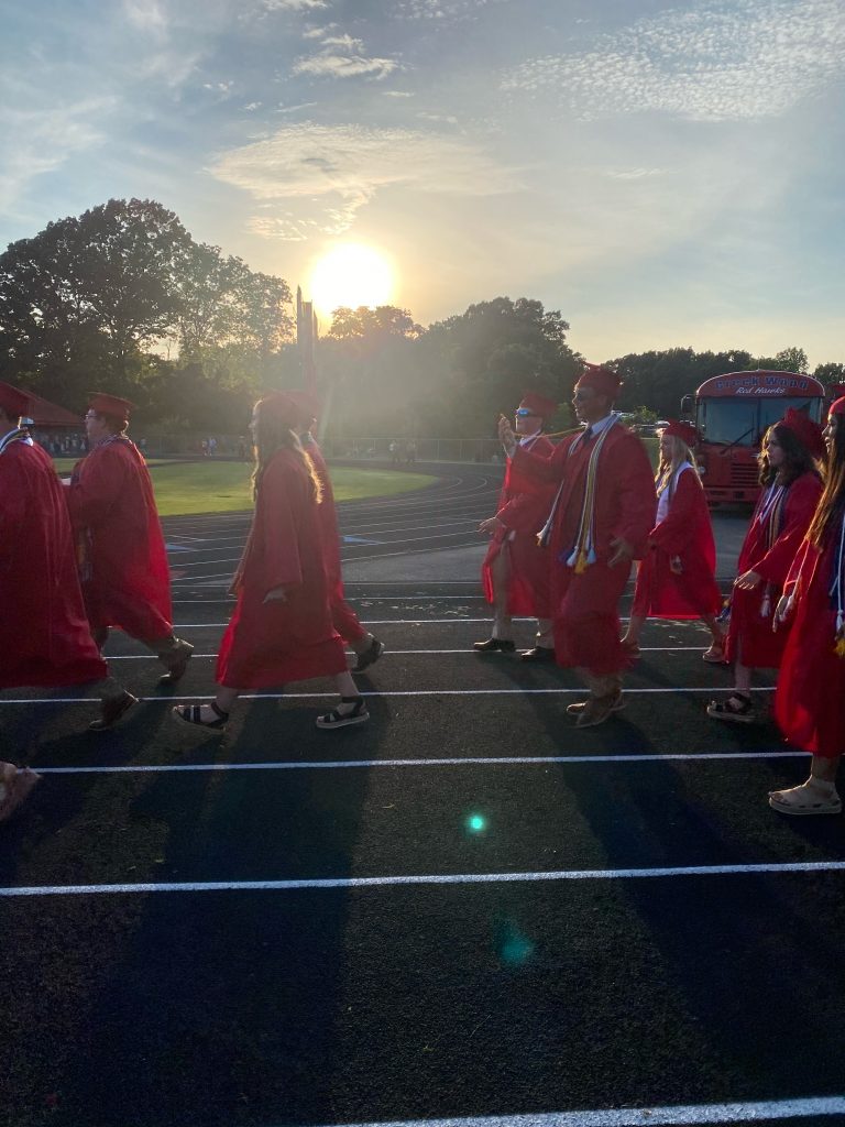 Graduating seniors in red gowns walking at sunset