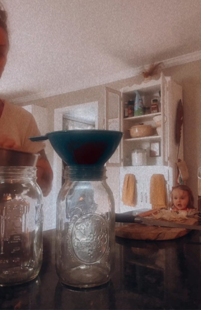 2 jars, one with a funnel sitting on a counter with pantry and baby in the background